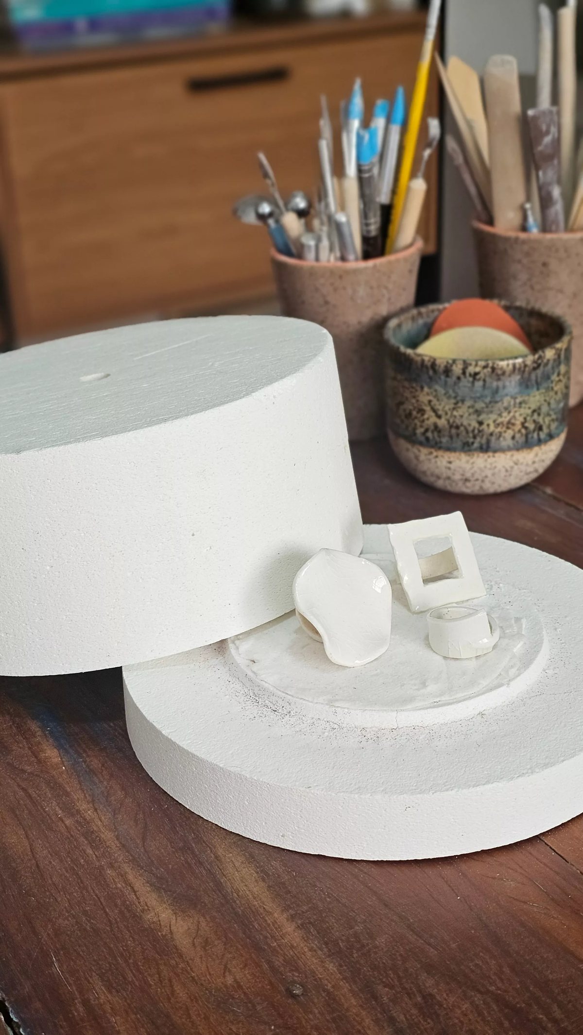 O ateliê da Korina: a mufla aberta, os pincéis e as ferramentas de cerâmica sobre a mesa de trabalho